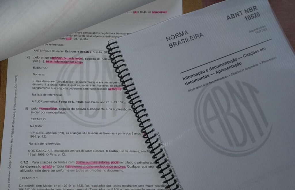Foto ilustrativa de cópias impressas da nova norma, sendo que uma delas tem trechos, ilegíveis, destacados em rosa.